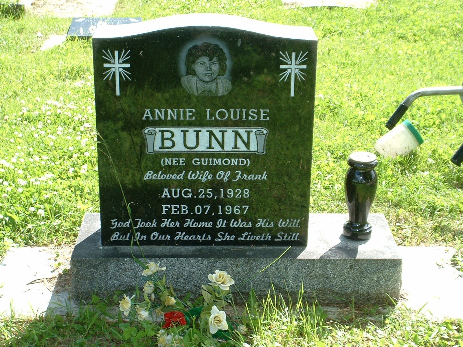 Black gravestone with engraved portrait and flowers in a grassy cemetery.