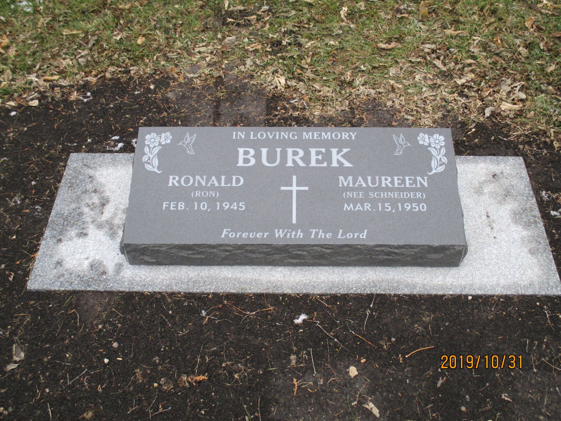 Gravestone on a concrete base in a wooded area, engraved “In Loving Memory BUREK” with cross and names Ronald and Maureen