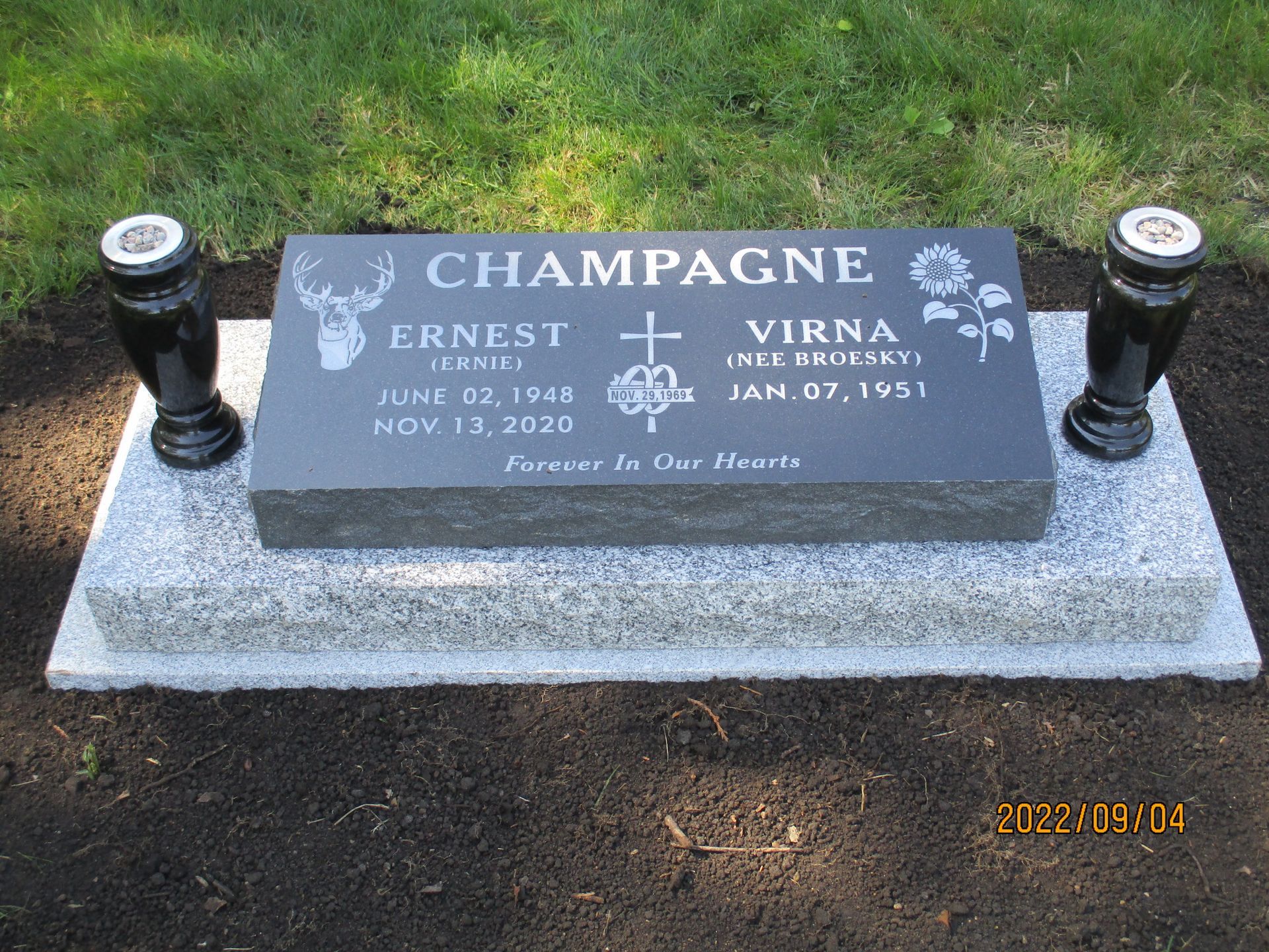 Champagne family gravestone with two black vases on a grassy cemetery plot