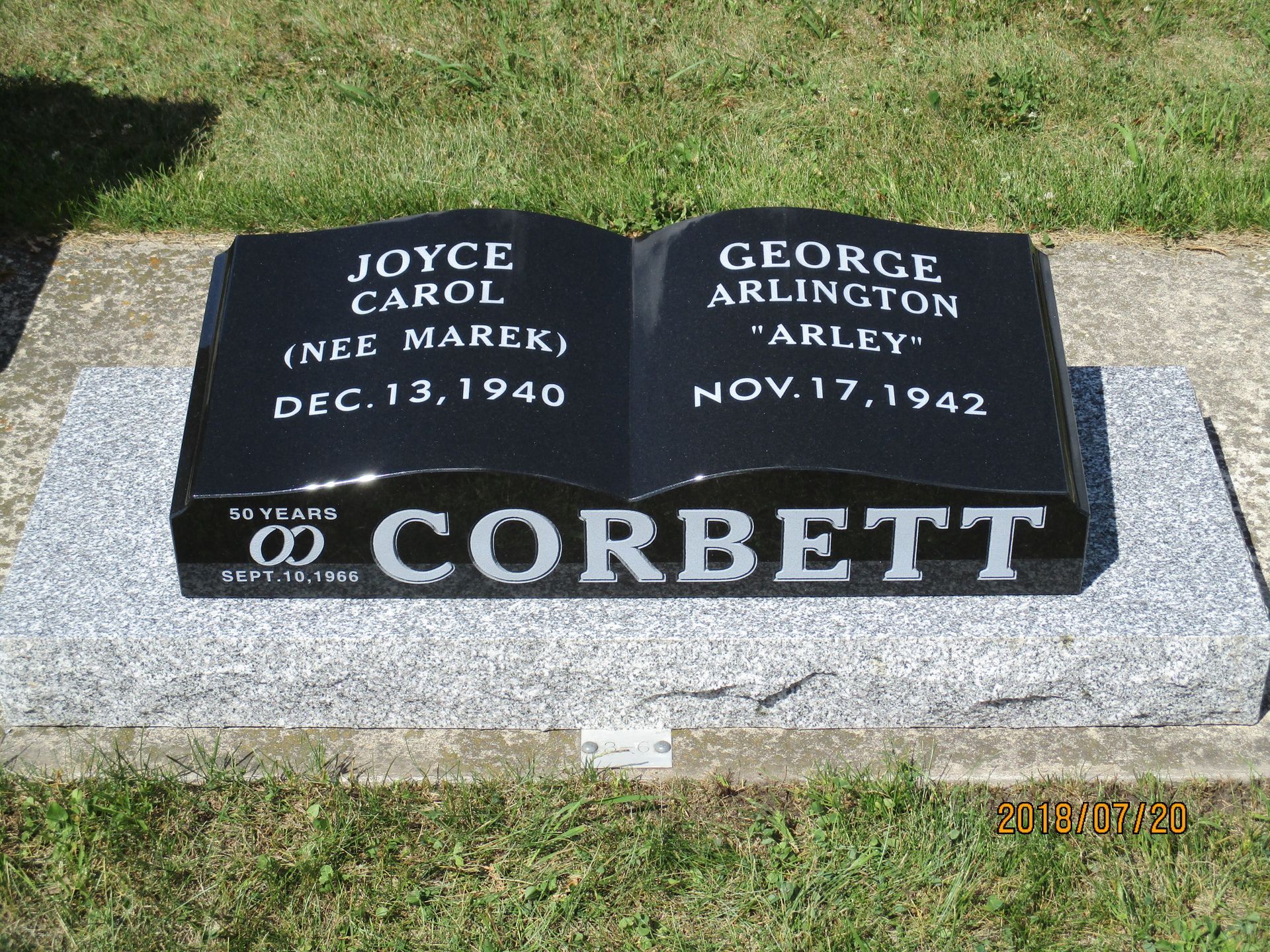 Gravestone with two black plaques on a gray marker in grass, for Joyce Carol Nee Marek and George Arlington Corbett