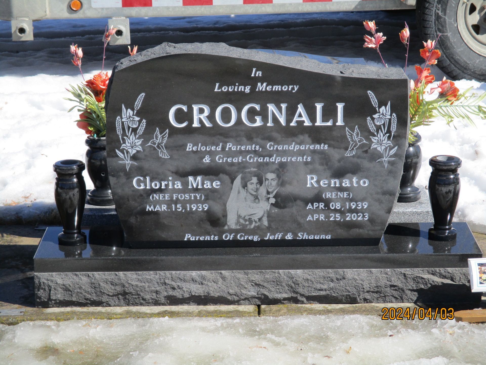Black granite gravestone with white engraved lettering and floral decorations on a cemetery plot