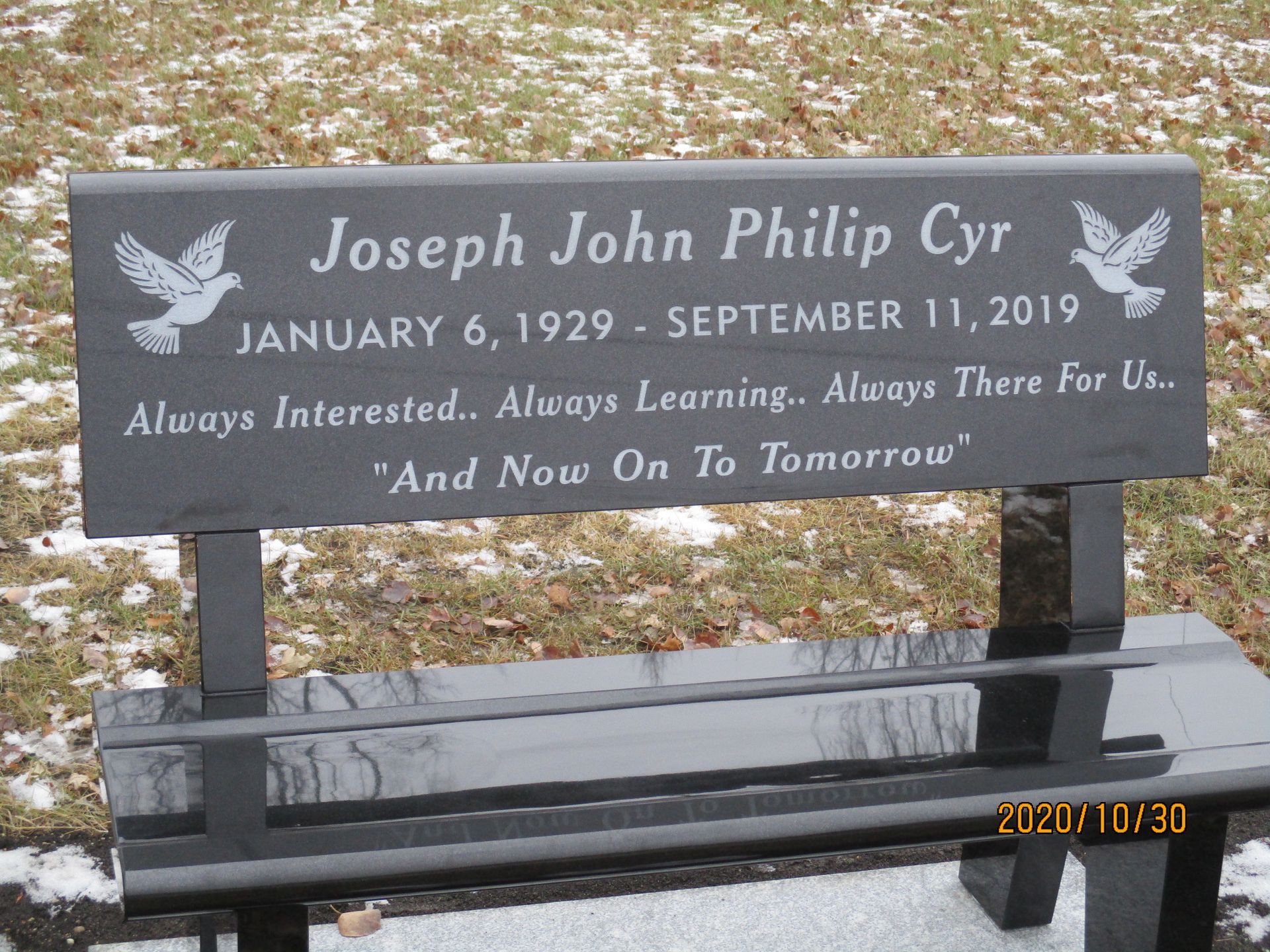 Memorial bench with plaque reading “Joseph John Philip Cyr” in a snowy outdoor setting