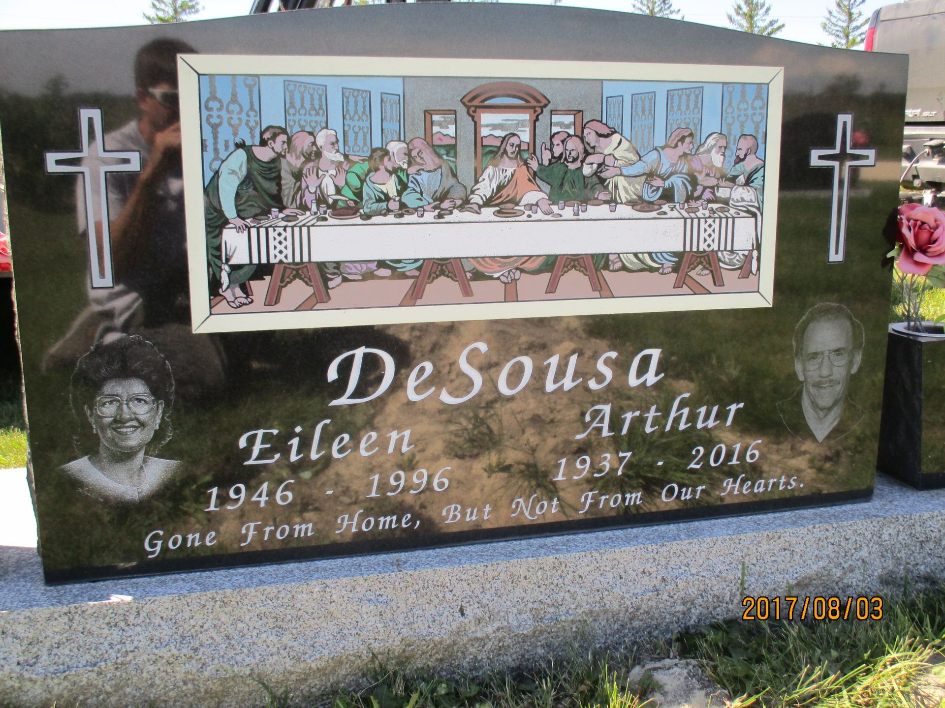 Gravestone for DeSousa and Arthur with a colorful Last Supper engraving and a cross on each side.