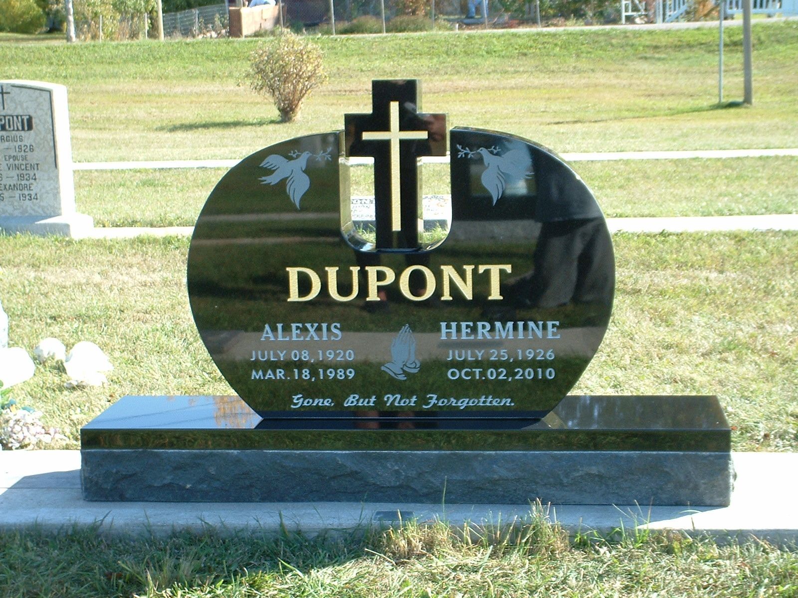 Black Dupont gravestone with gold cross in a grassy cemetery
