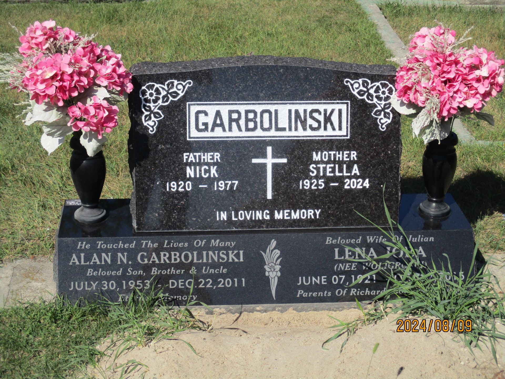 Black gravestone with pink flowers and the name Garbolinski in a cemetery.