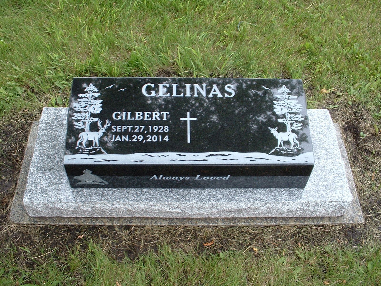Black granite gravestone with white lettering and cross, set on a concrete base in grass.