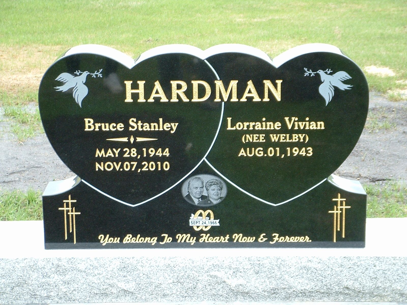 Black heart-shaped memorial headstone for the Hardman family on a grassy lawn with gold lettering and doves