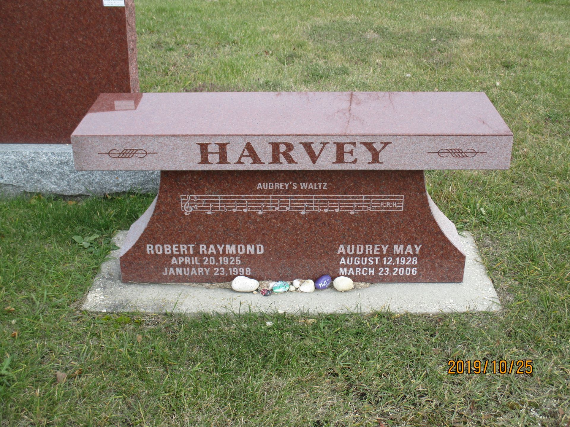 Gravestone bench with the name HARVEY in a grassy cemetery setting.