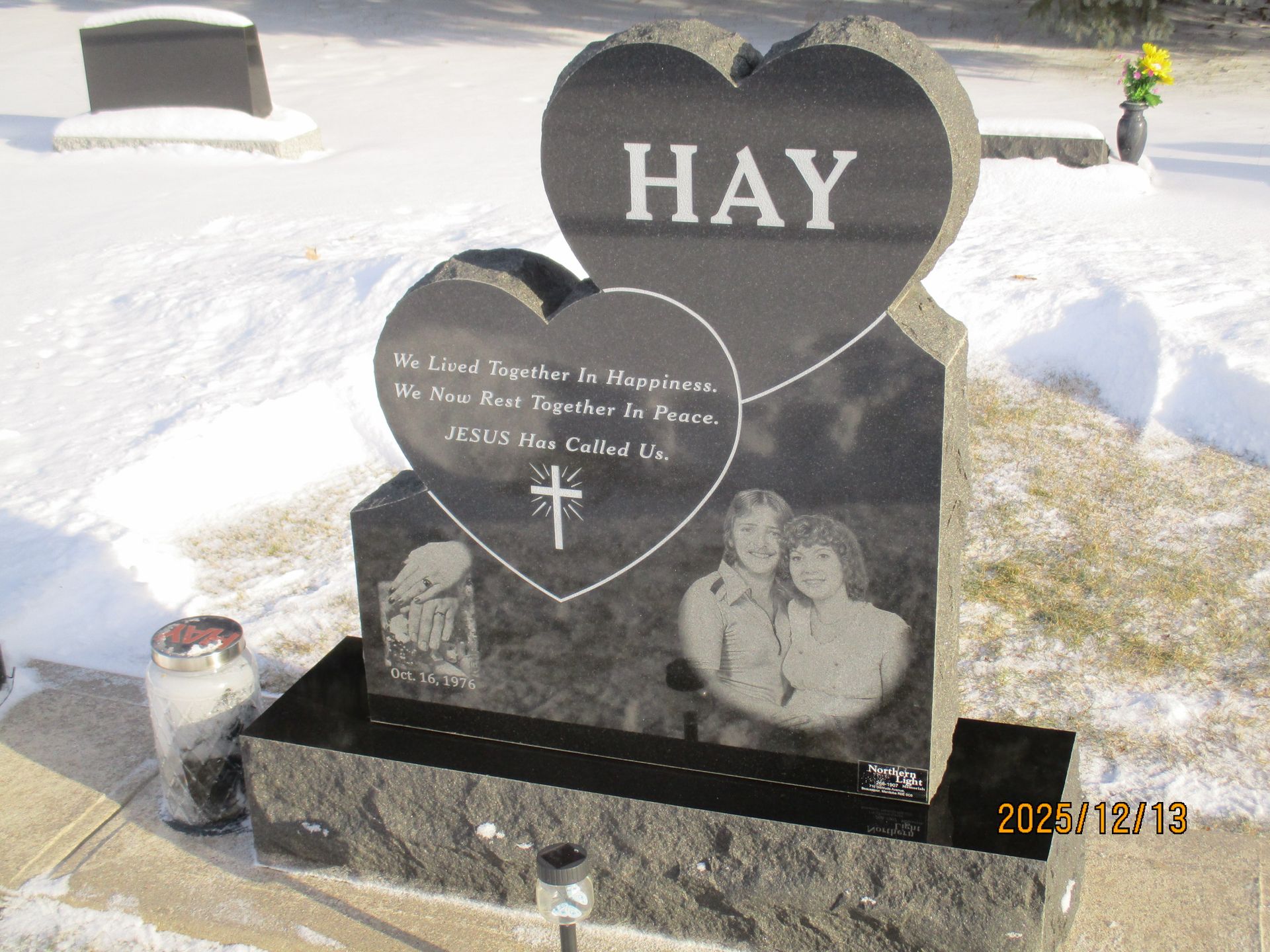 Heart-shaped black gravestone in snowy cemetery with the name HAY and etched memorial photos.