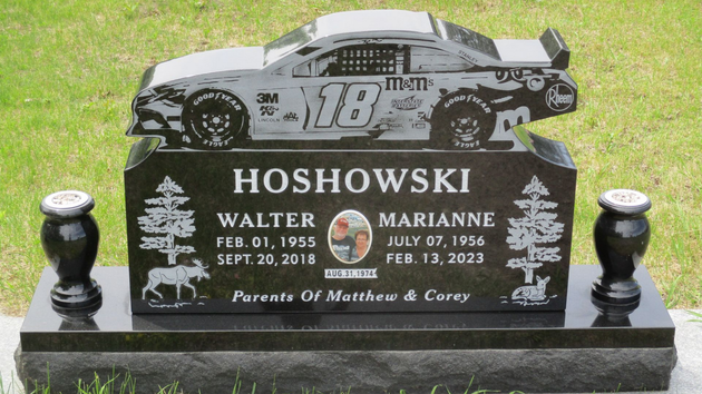 Black-and-white race car gravestone for Hosowski, with roses on a green lawn.