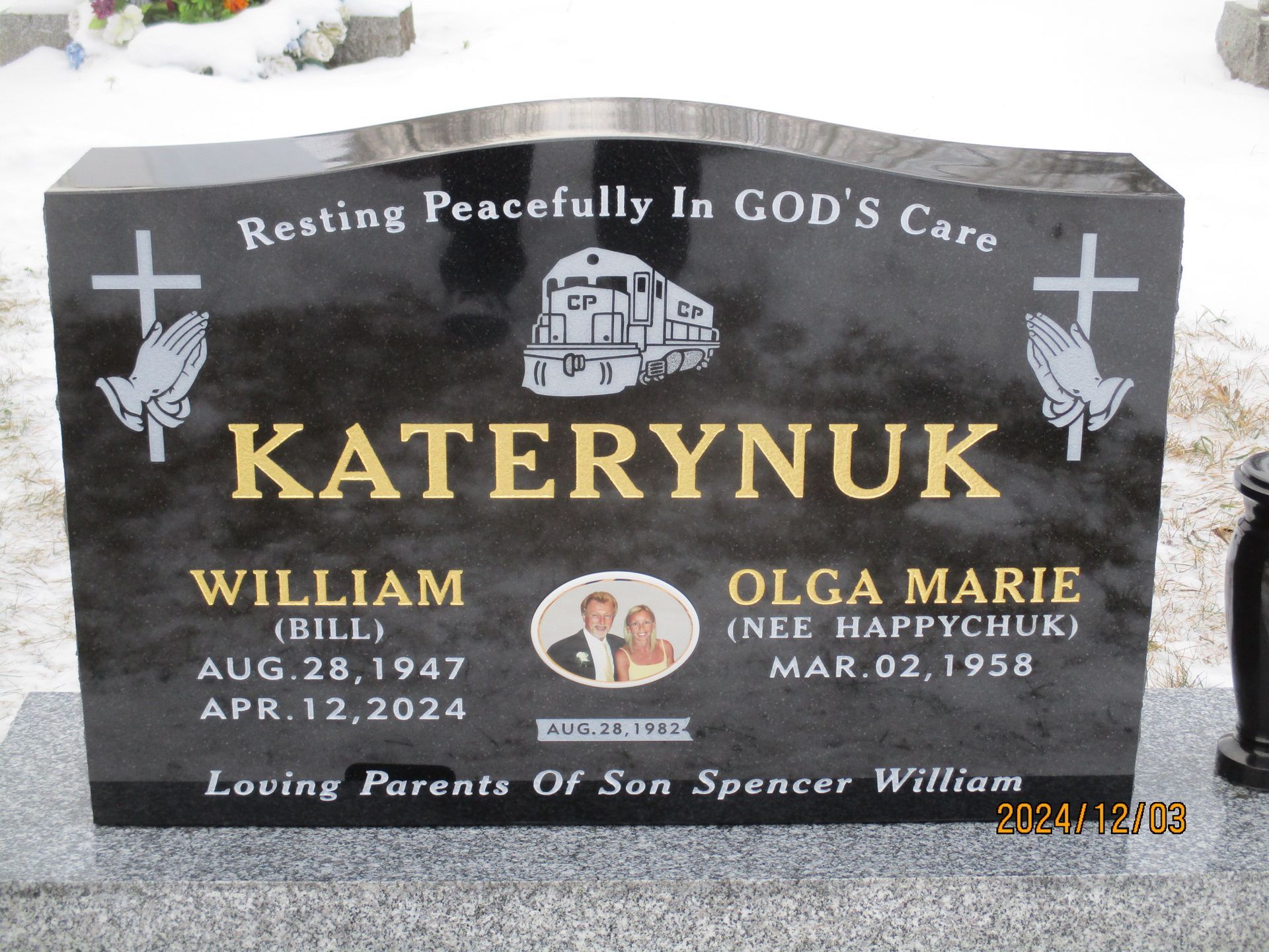 Gray memorial headstone with crosses and angel, reading “KATERYNIK” and “Resting Peacefully in GOD’s Care”