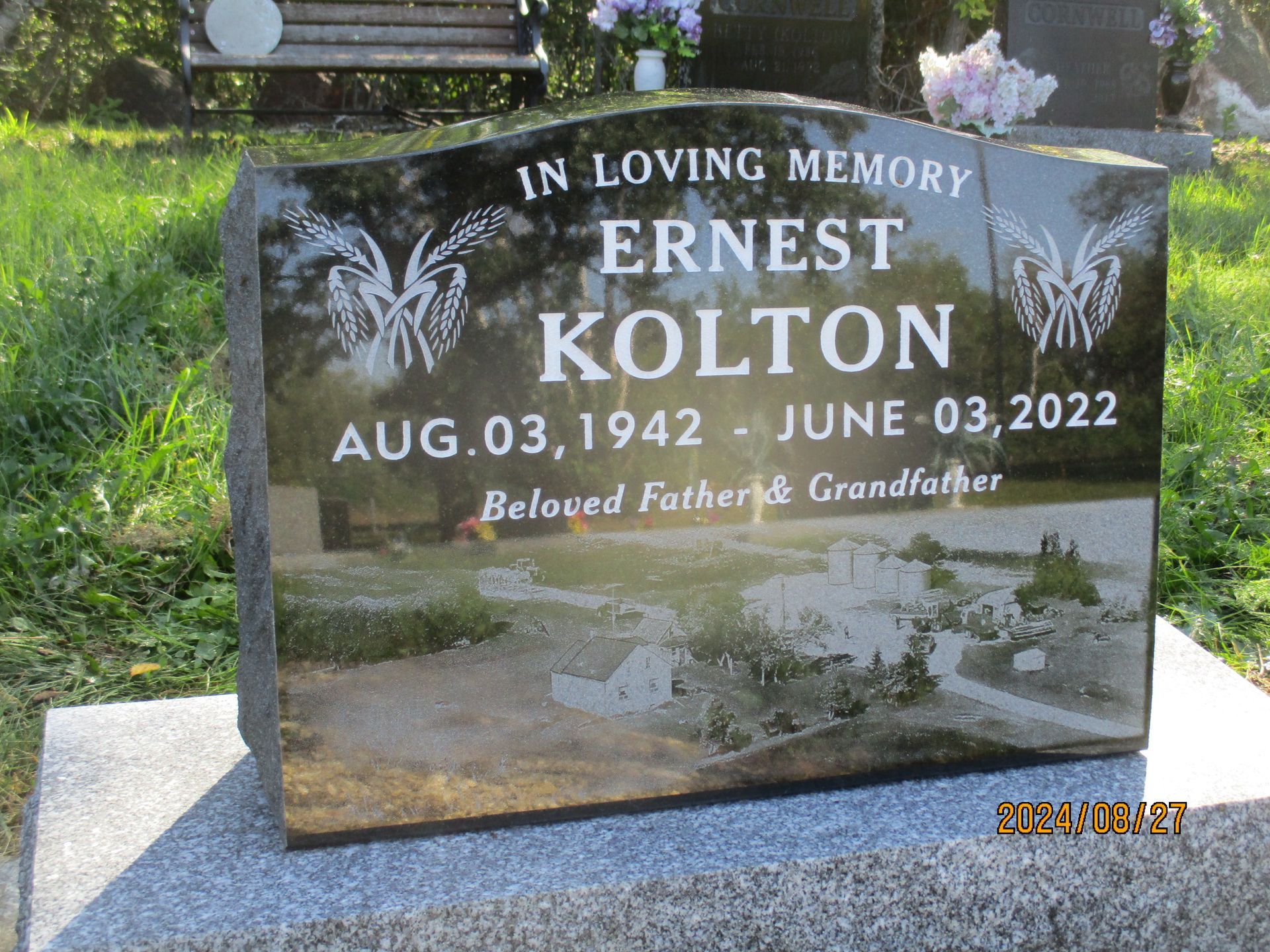 Gravestone for Ernest Kolton in a cemetery, with flowers and a glossy black stone.