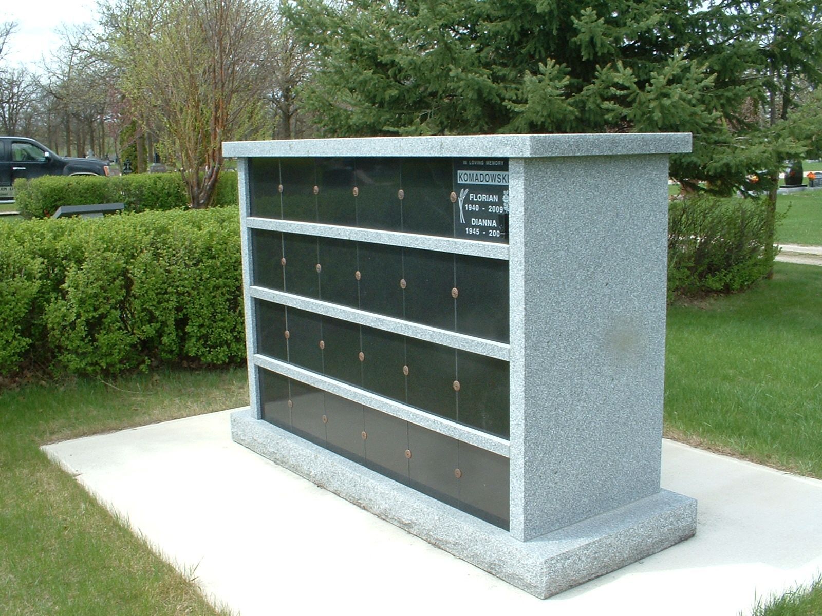 Memorial wall with engraved black plaques and a red wreath on a stone base outdoors