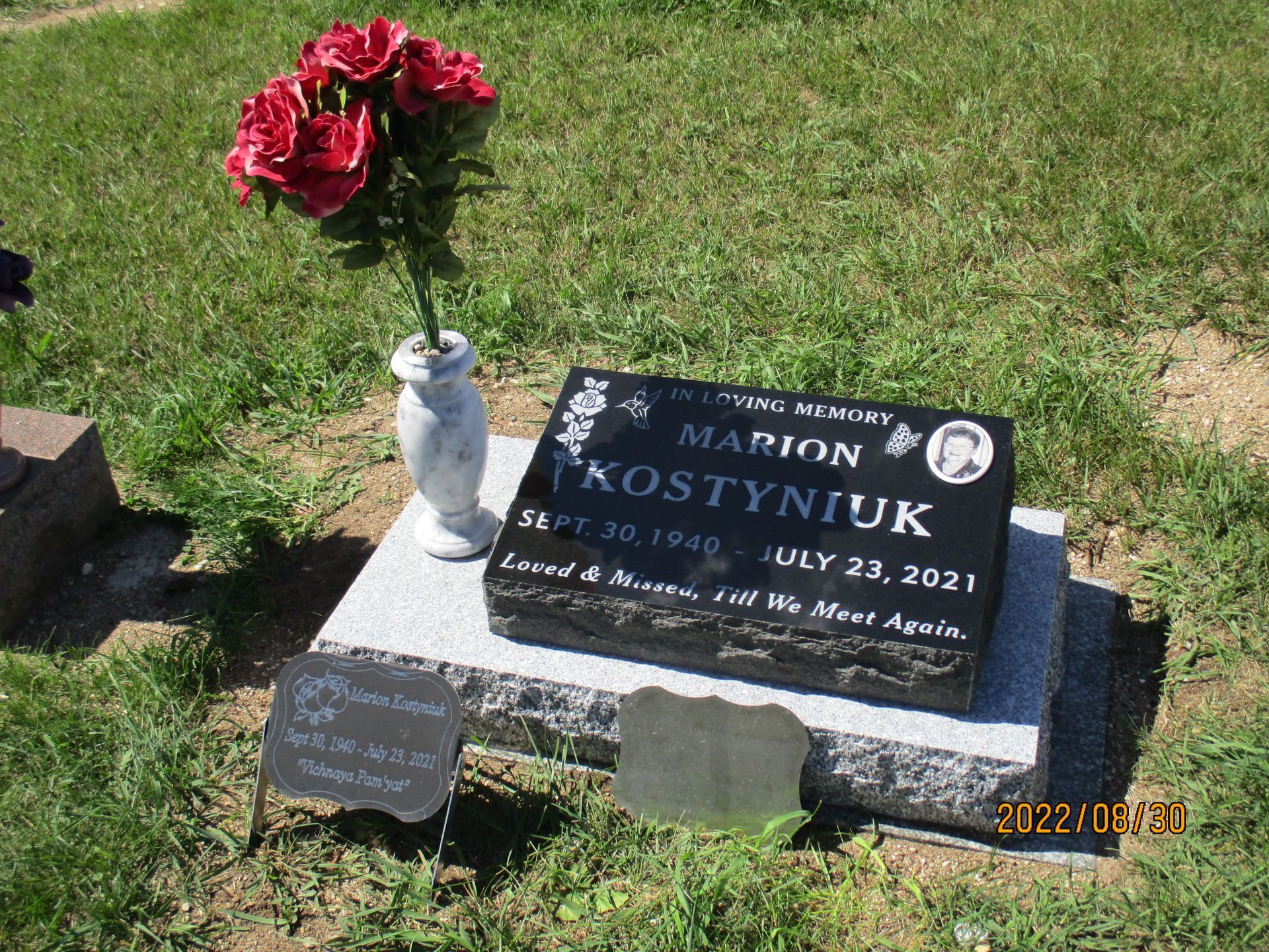 Gravestone with red flowers and a white vase in a grassy cemetery plot