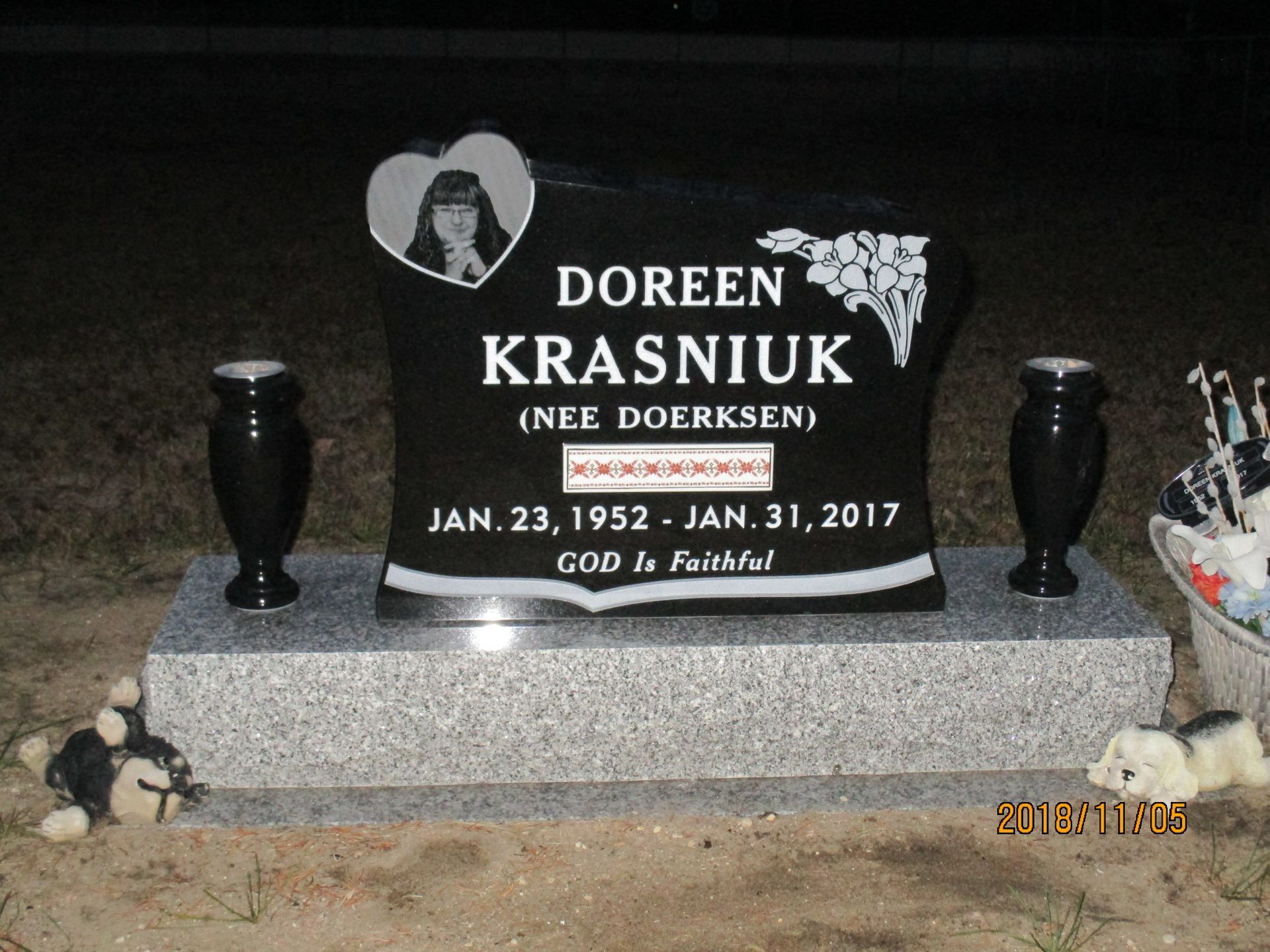 Black granite memorial headstone with portrait, flowers, and a small stuffed animal at the base.