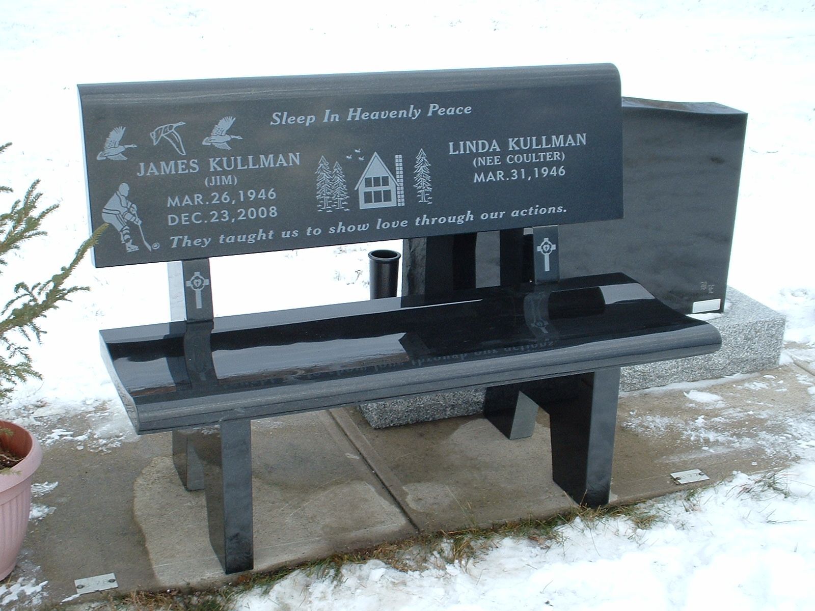 Memorial bench with engraved plaque and two black supports on a snowy outdoor path
