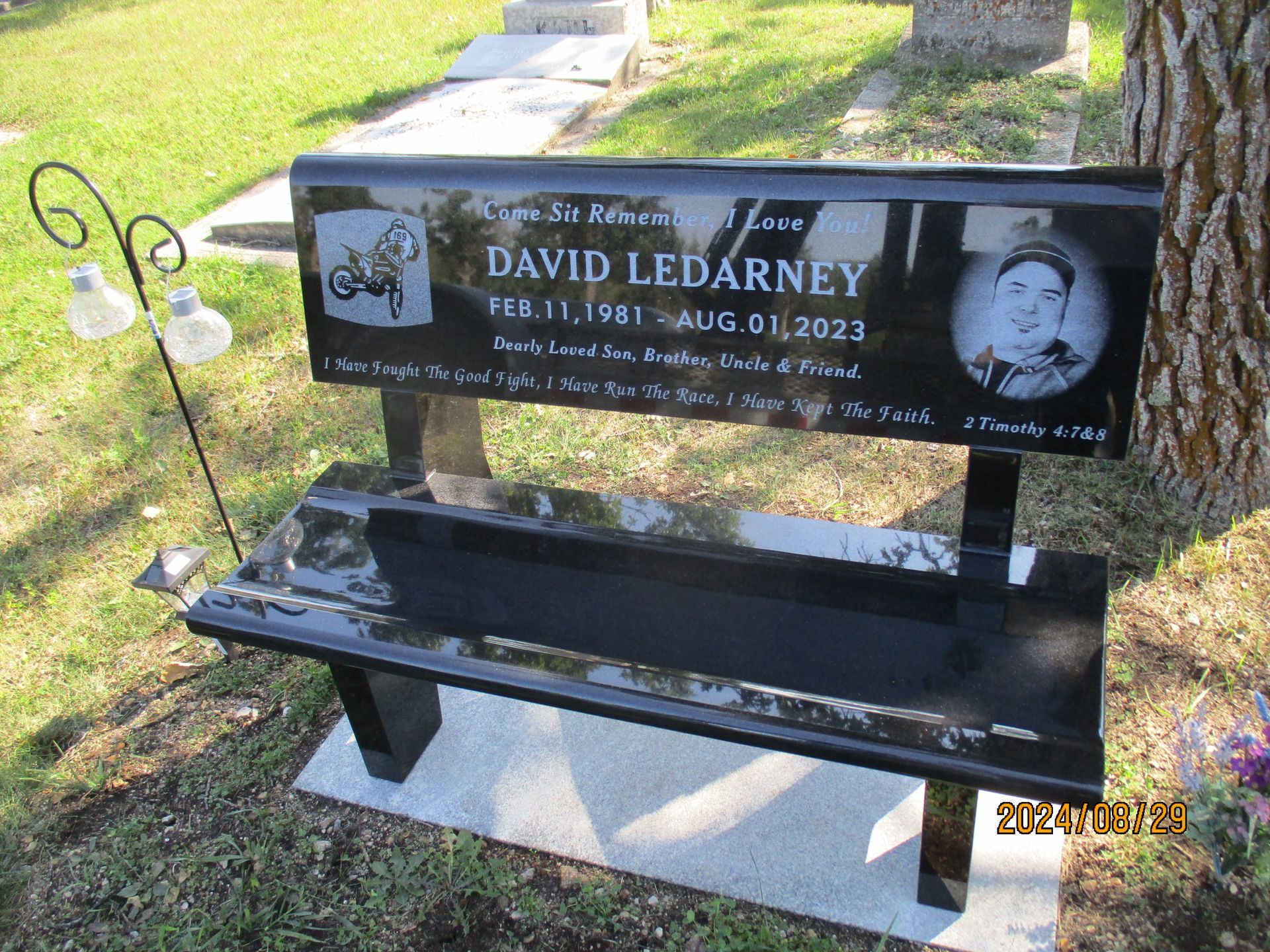 Black memorial bench and plaque for David Ledarmy in a grassy cemetery setting