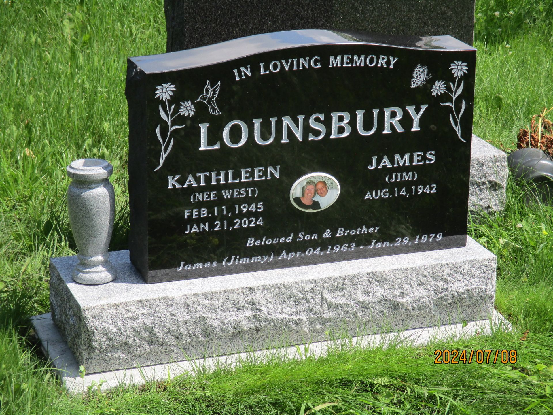 Black granite gravestone in grass engraved “Lounsbury” with flowers and names Kathleen and James.