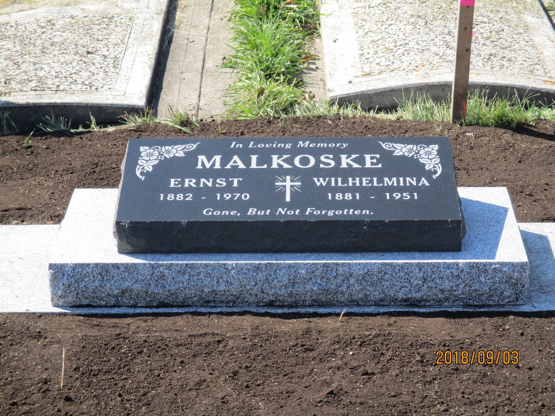 Gravestone for Ernst and Wilhelmina Malkose with flowers and a cross, set in a cemetery.