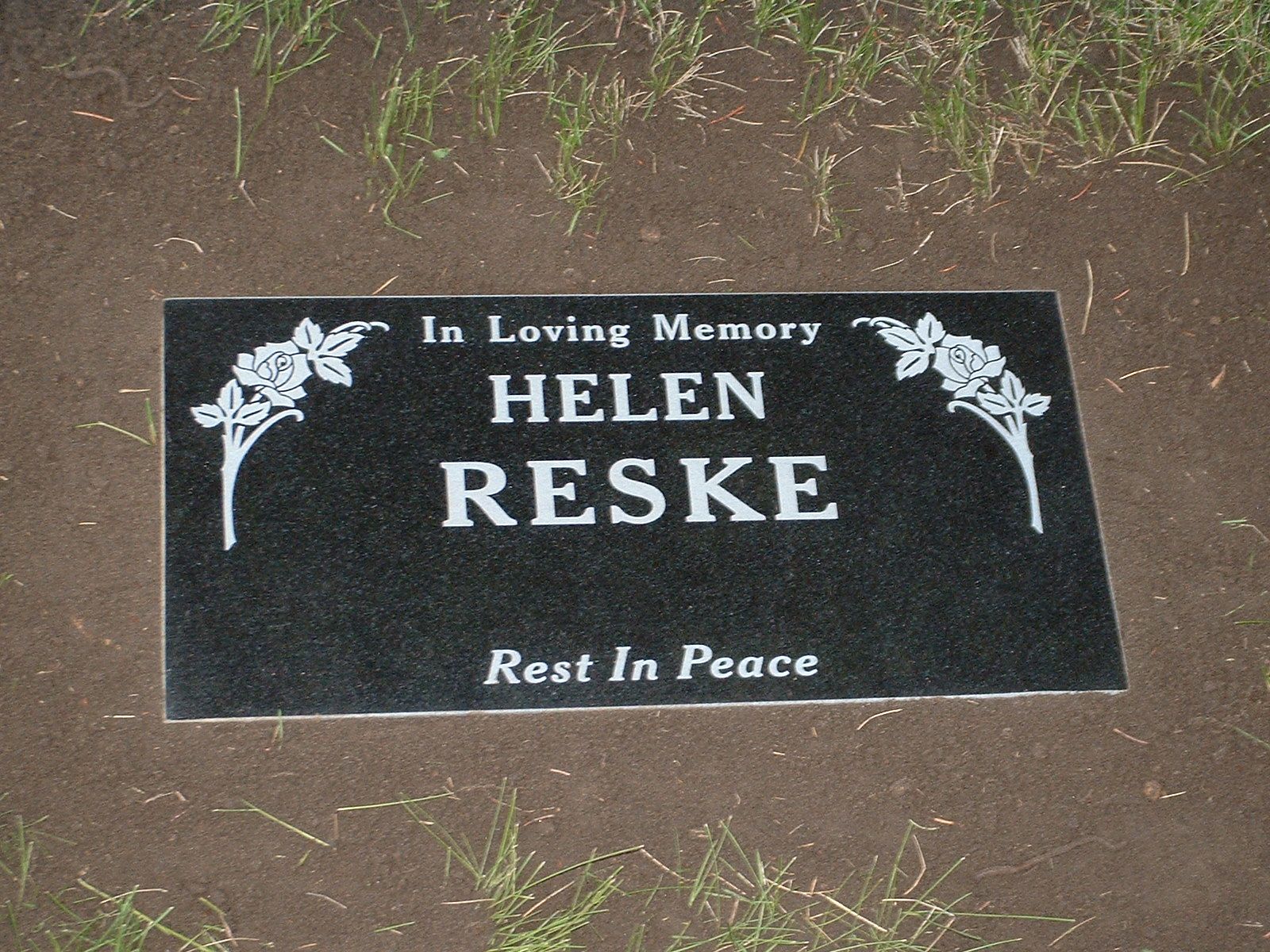 Black memorial plaque in dirt reading “In Loving Memory Helen Reske” and “Rest In Peace”