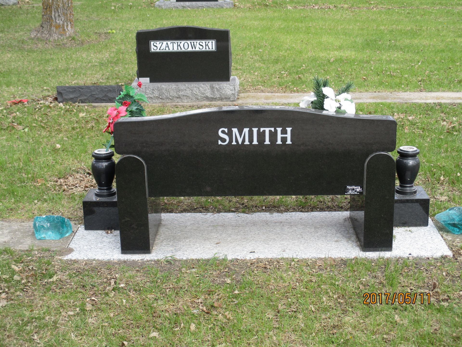 Black gravestone marked “SMITH” with flowers in a grassy cemetery.