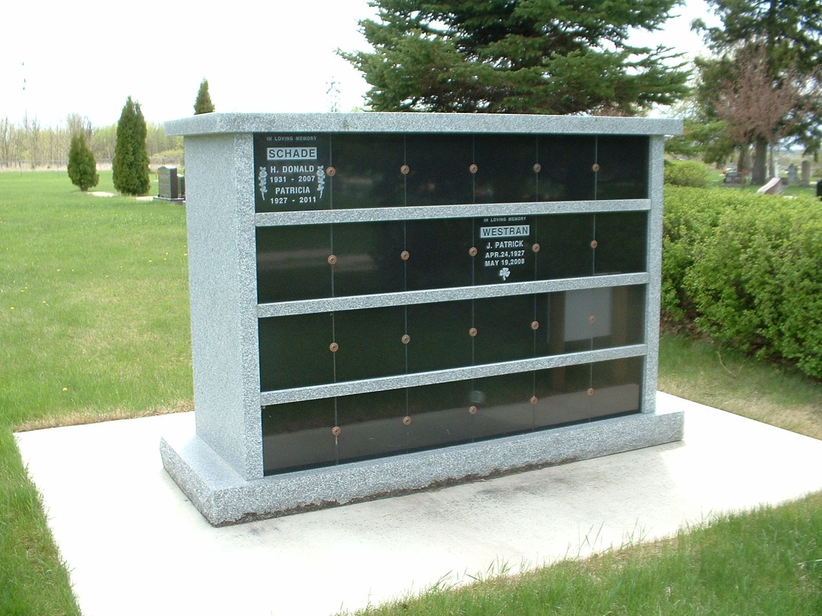 Cedar columbarium niche with granite exterior and black plaque in a cemetery
