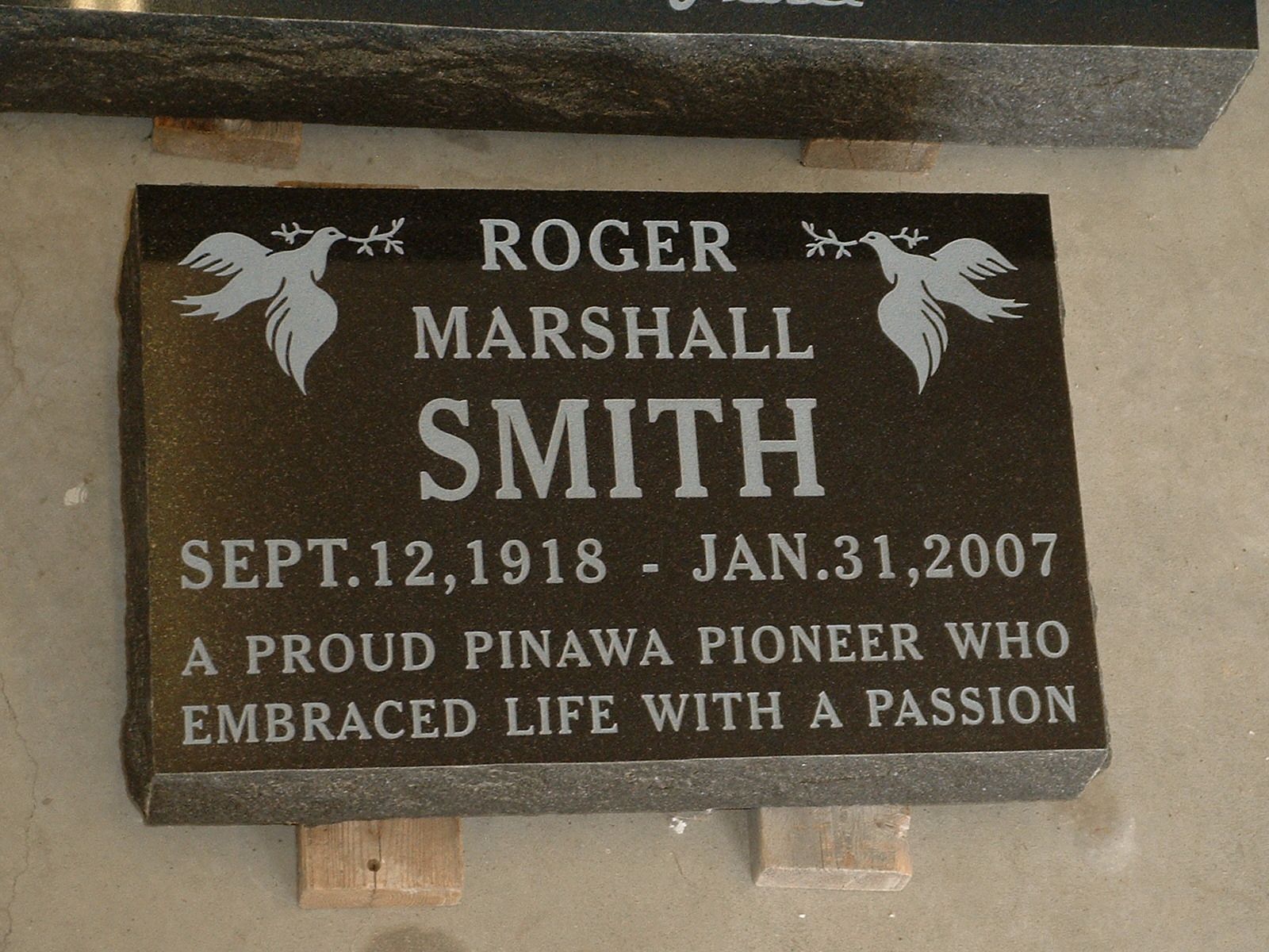 Black memorial plaque for Roger Marshall Smith with white engraved text and two angels