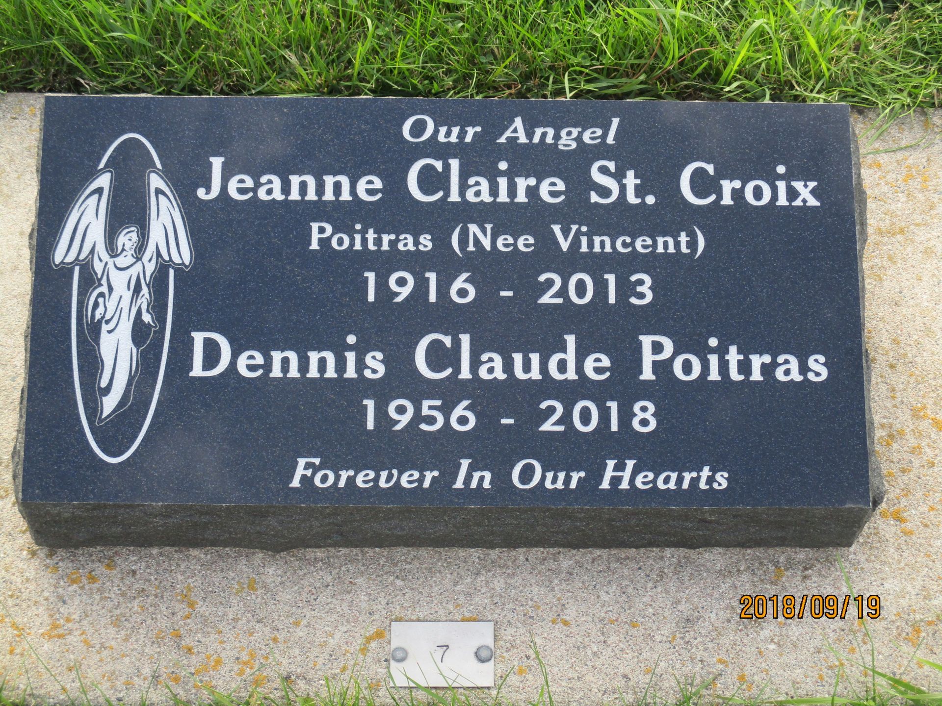 Black memorial plaque in grass honoring Jeanne Claire St. Croix and Dennis Claude Poitras with angel engraving.