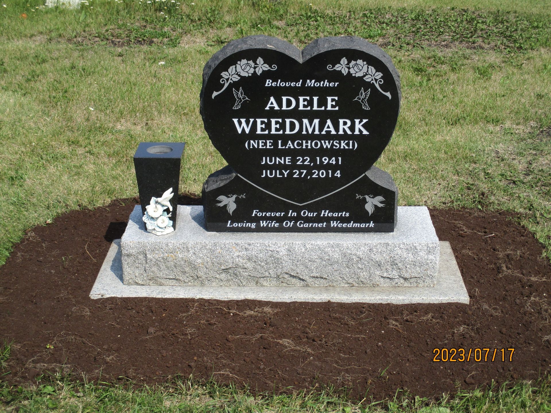 Black gravestone for Adele Wedmark on a concrete base in a grassy cemetery.