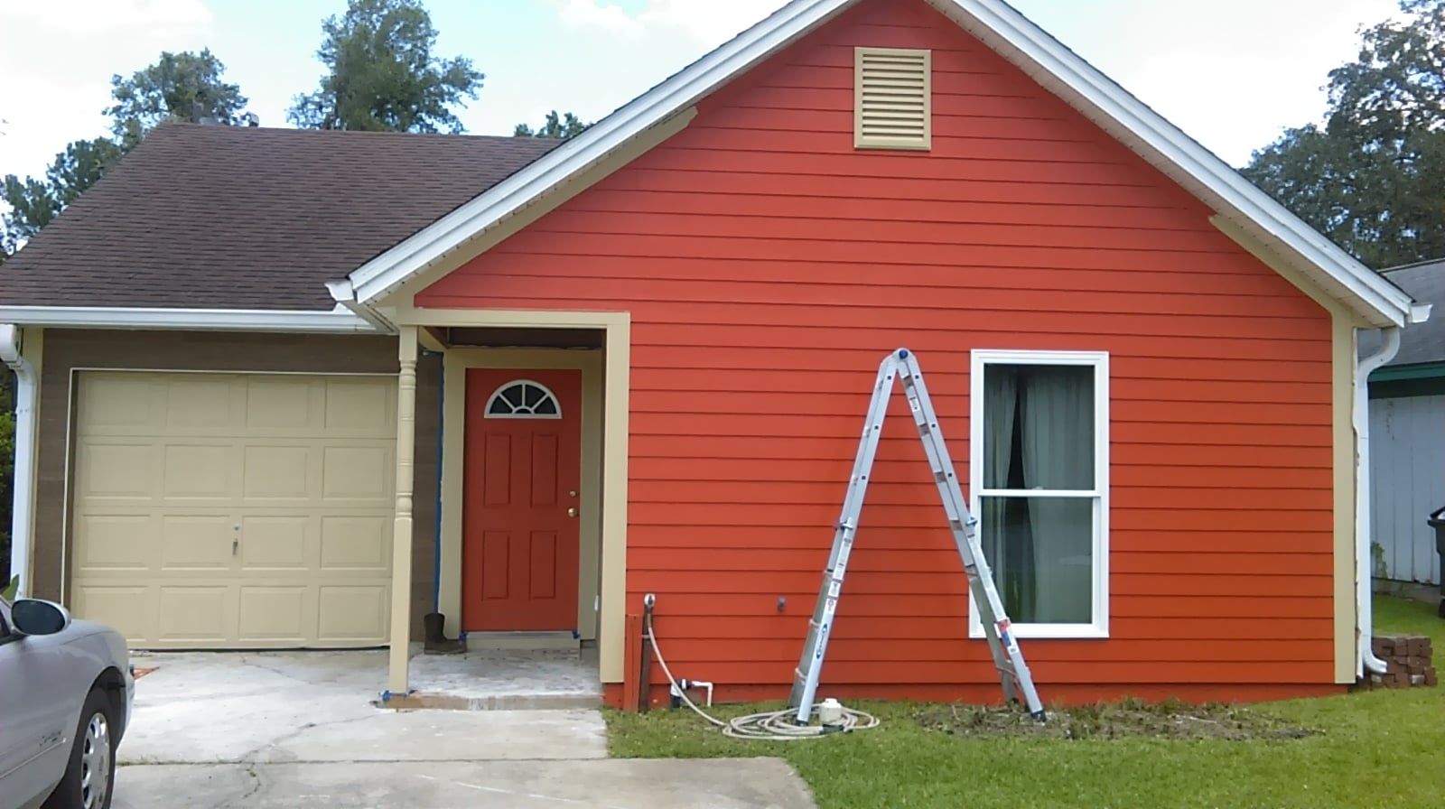 Red house with beige garage, door, and trim. Ladder leans against the red wall next to a window.