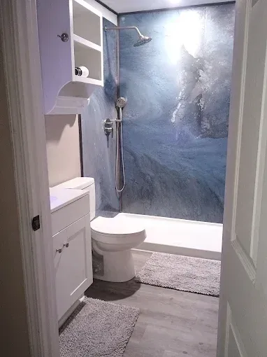 Bathroom with a blue and white shower, white cabinets, and a toilet.