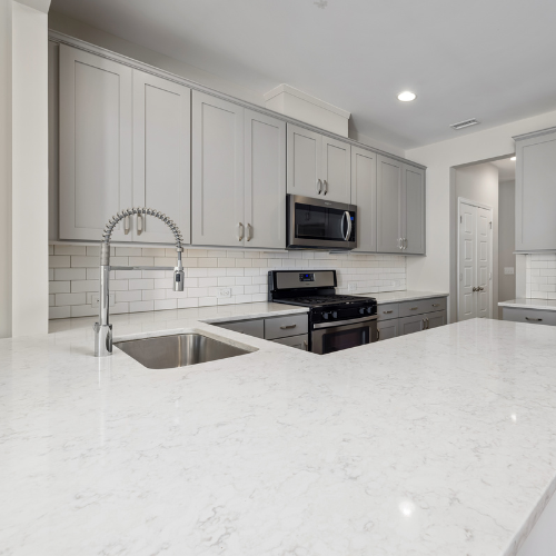 Modern kitchen with gray cabinets, white countertops, stainless steel appliances, and a tile backsplash.