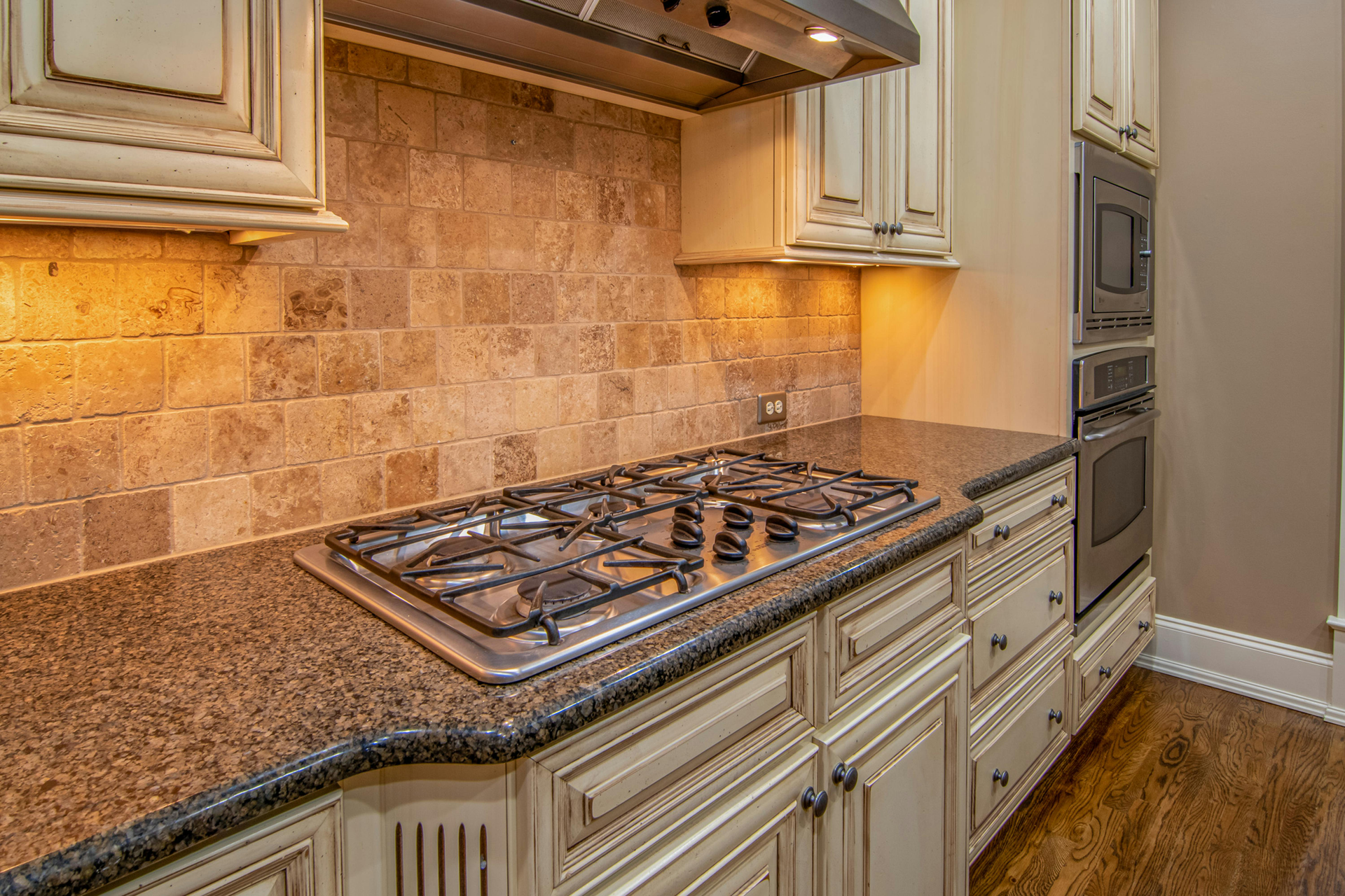 Kitchen with cream cabinets, gas cooktop, stone backsplash, granite countertop.