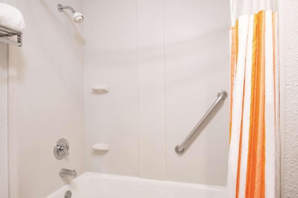 A bathroom with a bathtub , shower , and handrails.