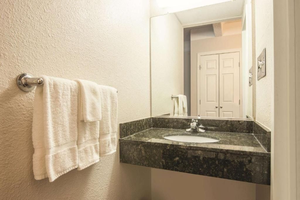 A bathroom with a sink , mirror and towels hanging on the wall.