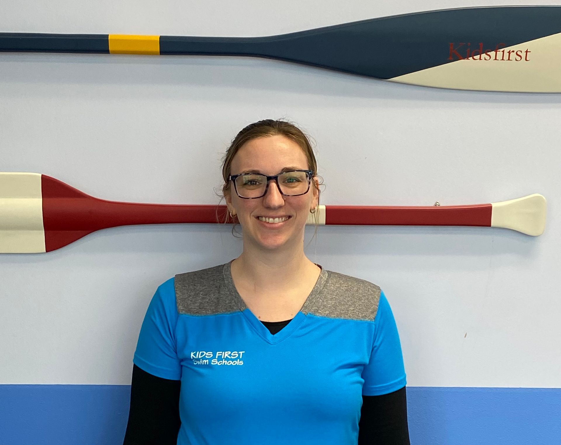 A woman in a blue shirt is standing in front of two oars on a wall.
