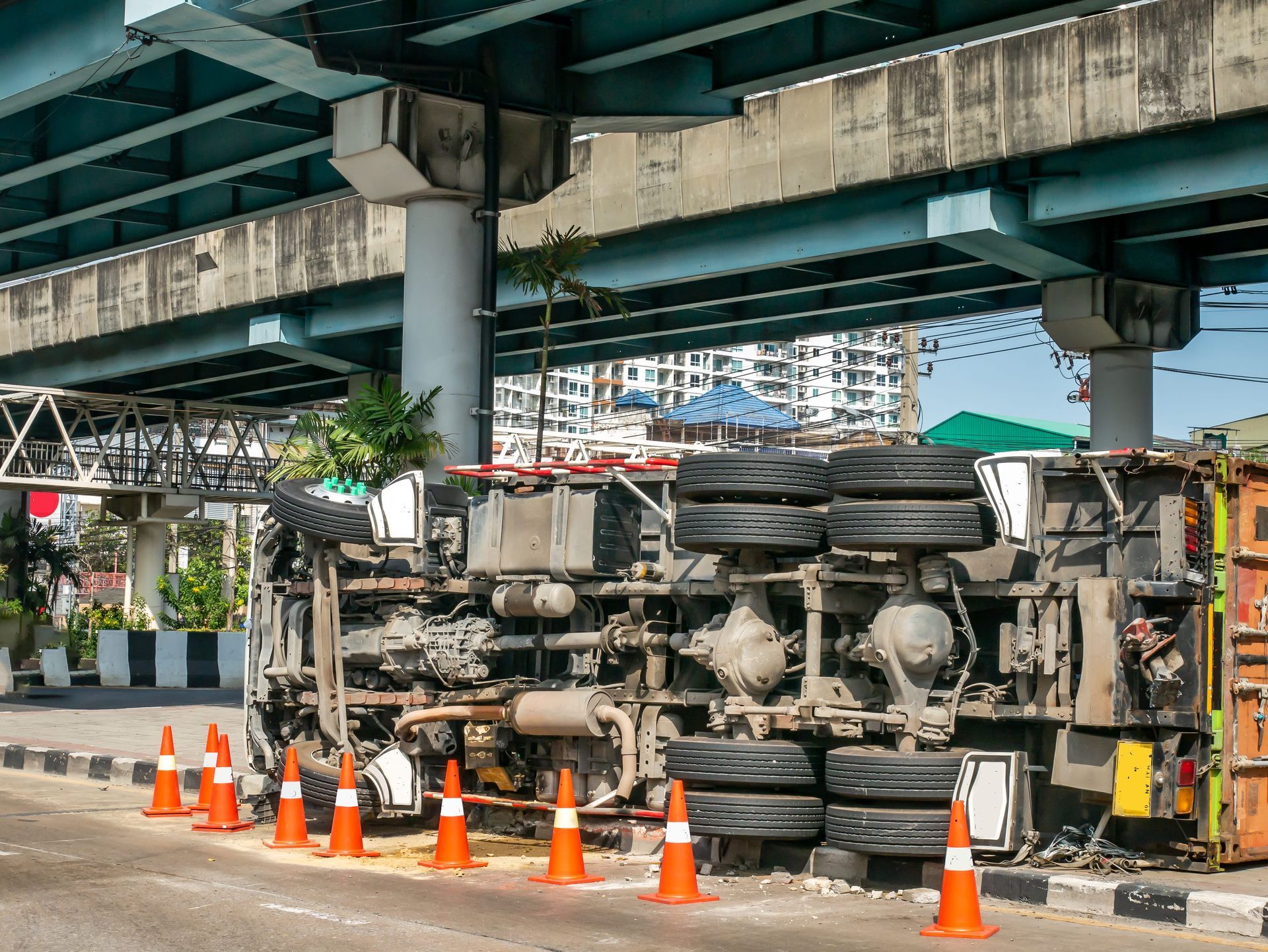 Overturned truck under an overpass, with orange cones marking the roadside scene