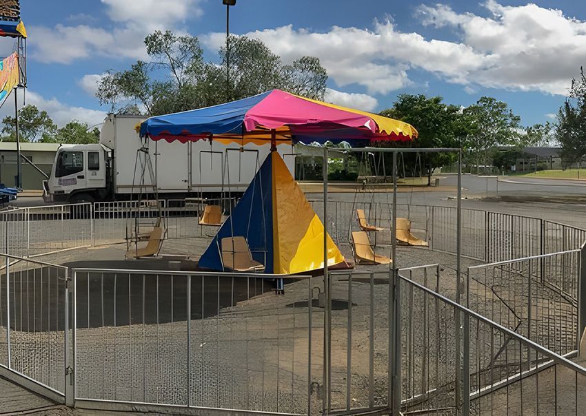 A Colourful Umbrella is in the Middle of a Fenced in Area — Fun Time Amusements in Gracemere, QLD