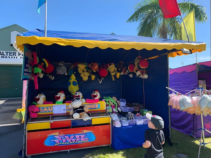 A Little Boy is Standing in Front of a Carnival Booth — Fun Time Amusements in Hervey Bay, QLD