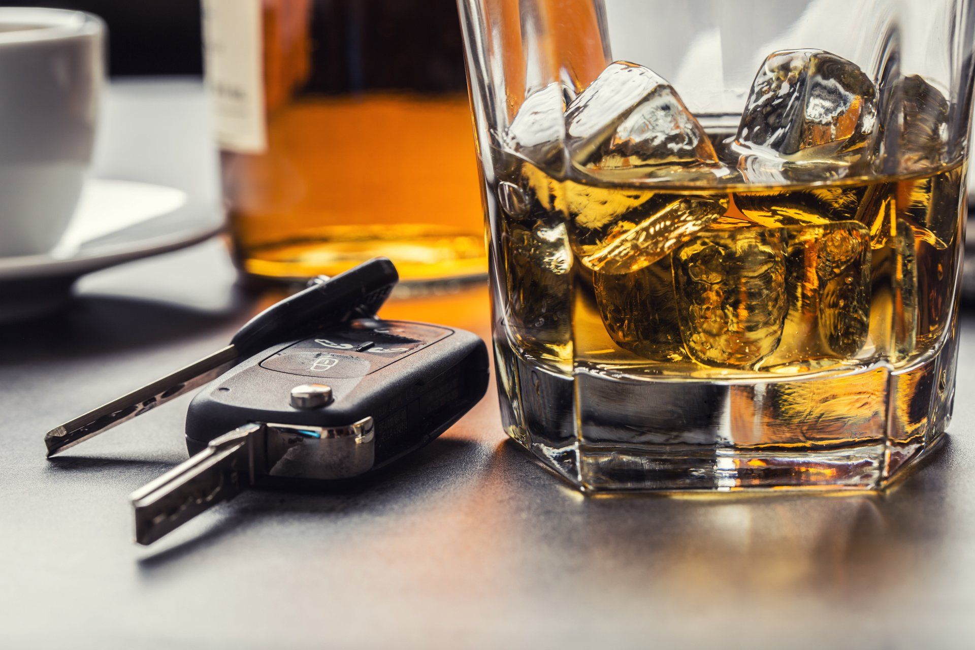 Car keys beside a glass of whiskey on a bar table, with another drink blurred in the background
