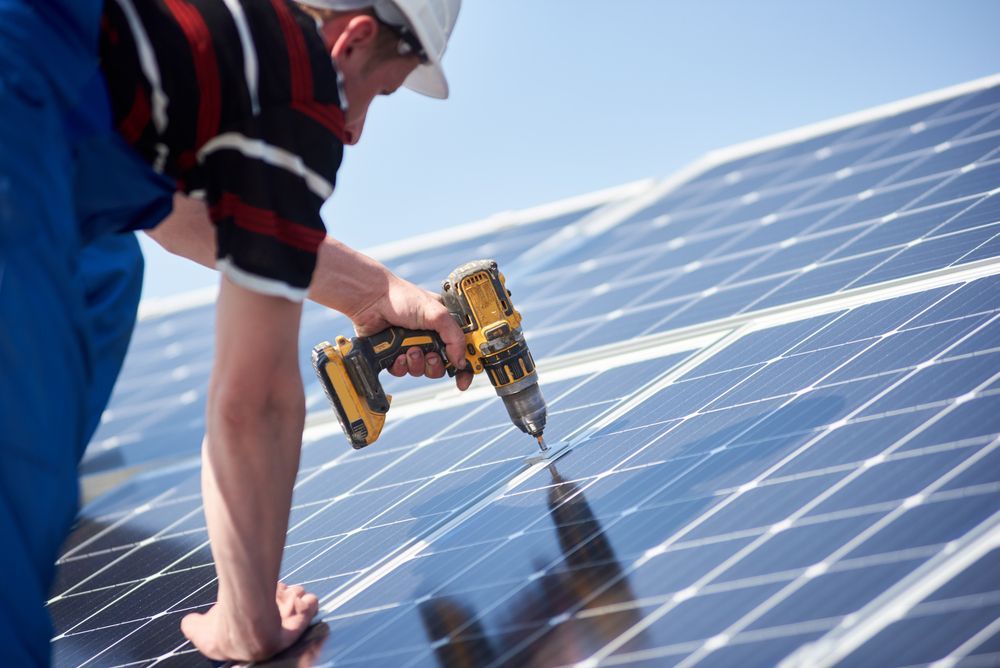 Worker Drilling Solar Panels on A Rooftop Under a Blue Sky — Local Light Electrical in Suffolk Park, NSW