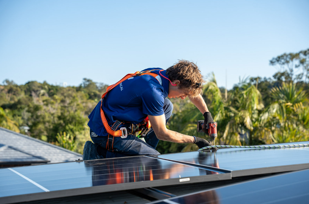 Worker Standing on Solar Panels on a Rooftop Under Bright Sunlight — Local Light Electrical in Suffolk Park, NSW