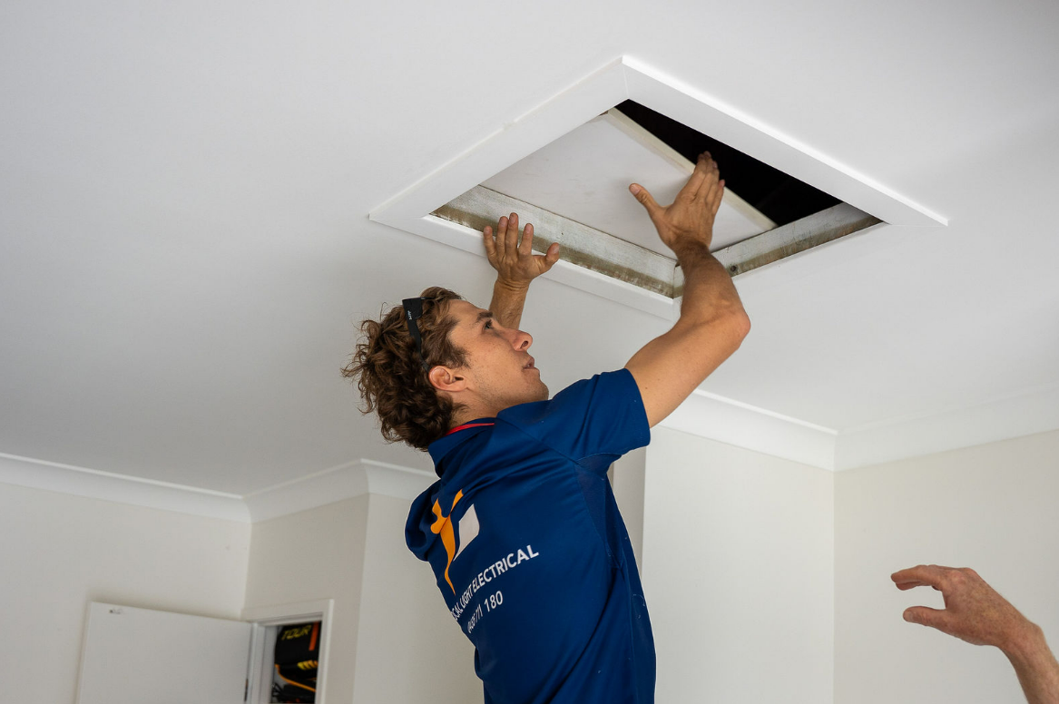 Worker Installing an Electric Power on An Attic White Ceiling — Local Light Electrical in Ocean Shores, NSW