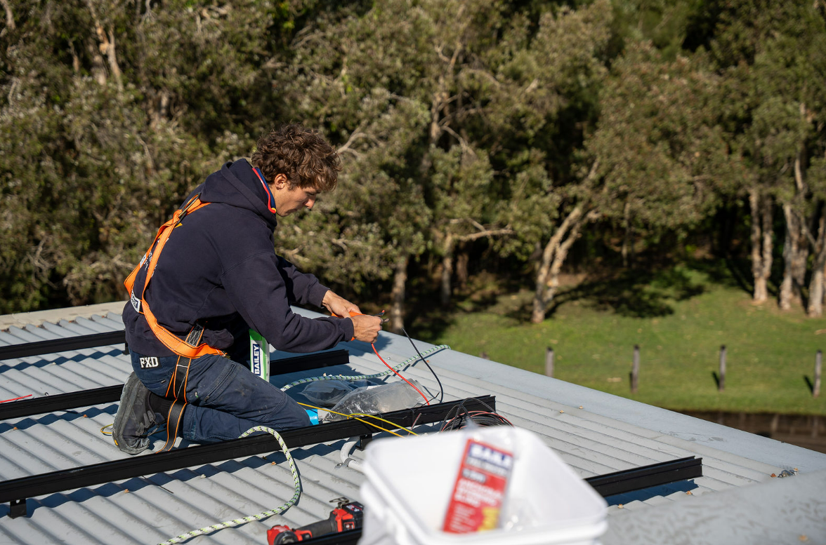 Worker on A Rooftop Installing Solar Panels, with Tools and Wiring — Local Light Electrical in Mullumbimby, NSW