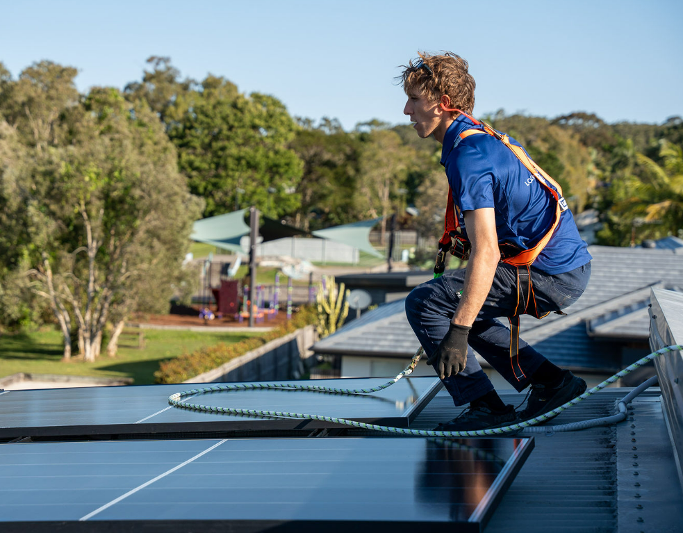 Worker in Blue Safety Gear Cleaning Solar Panels on a Rooftop — Local Light Electrical in Suffolk Park, NSW