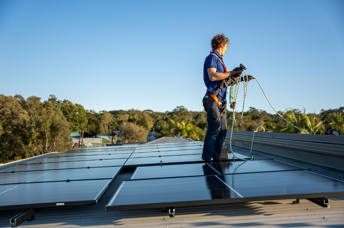 Worker inspecting solar panels on a rooftop under a blue sky