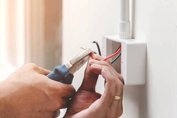 Hands Using Pliers to Connect Red and Black Wires in A Wall Electrical Box — Local Light Electrical in Suffolk Park, NSW