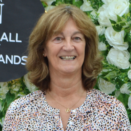 A woman is smiling in front of a wall of flowers.