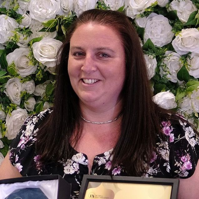 A woman is holding a framed picture in front of a wall of flowers.