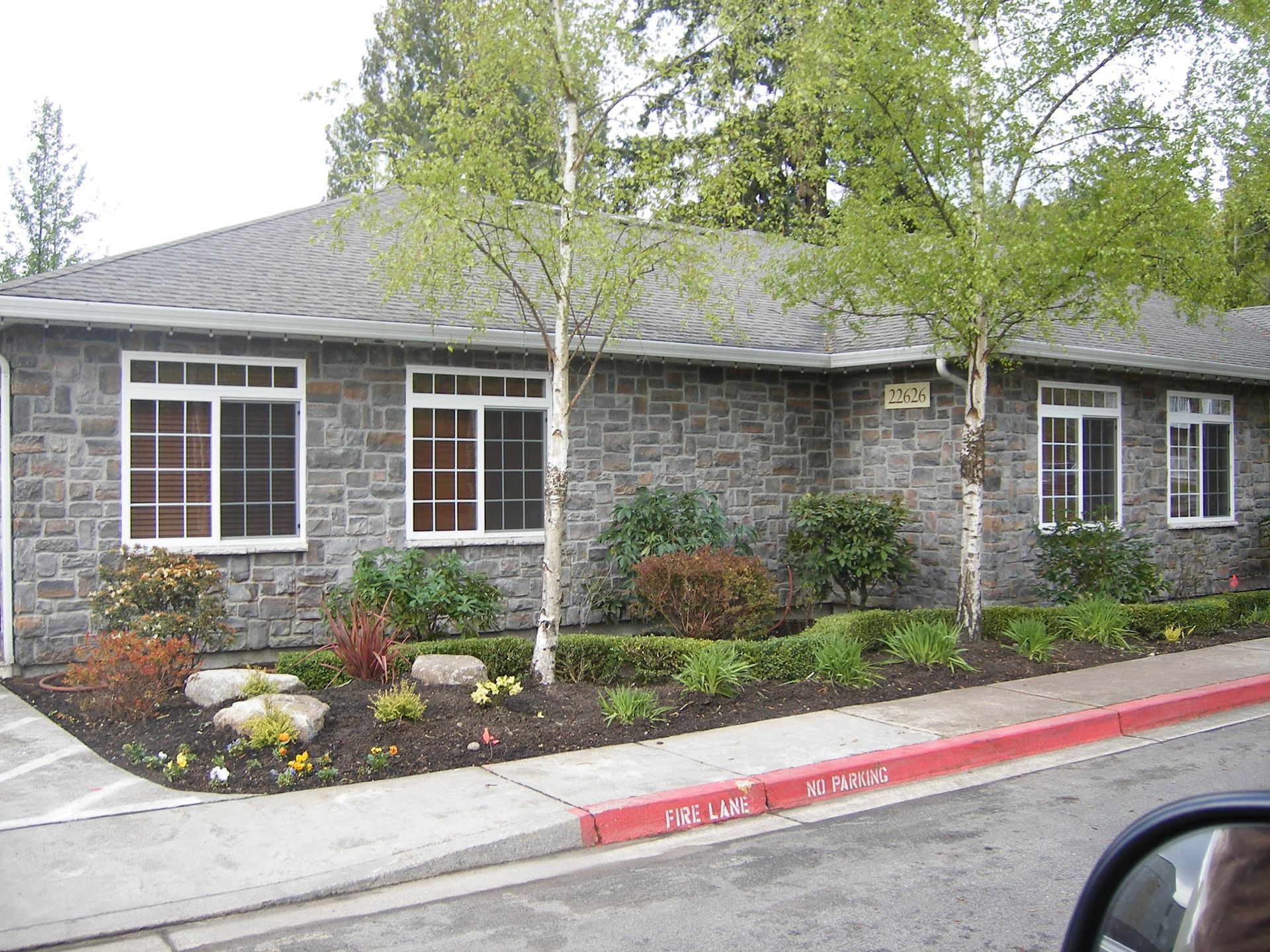 Stone office building with large windows, shrubs, and a red curb along the sidewalk